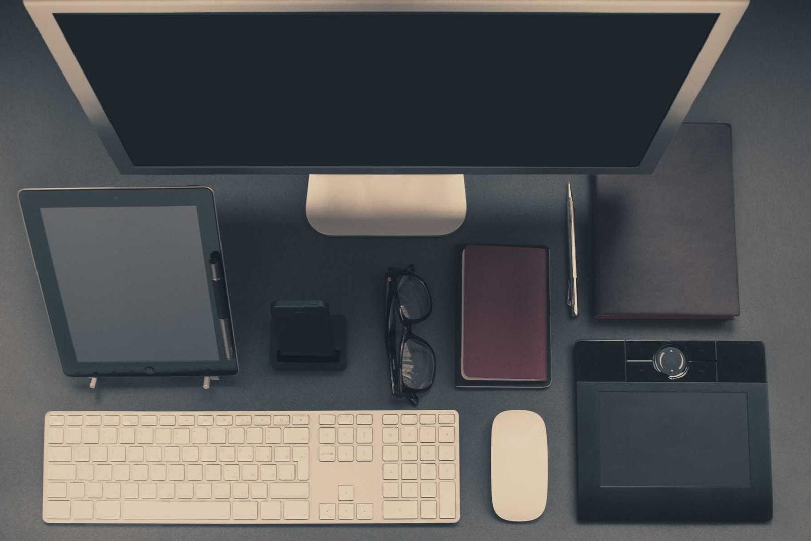 Desktop computer, tablet and keyboard arranged on a dark desk